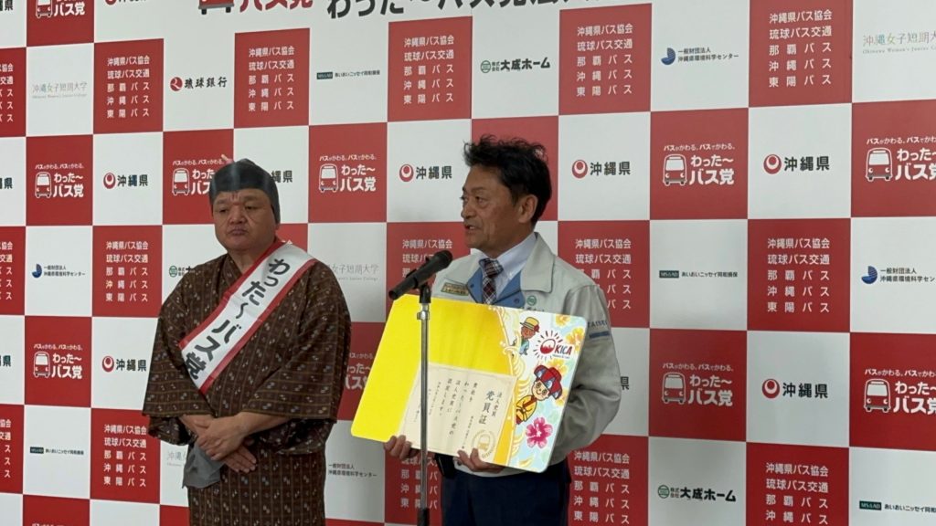 わったーバス党の党員証を手にスピーチする様子